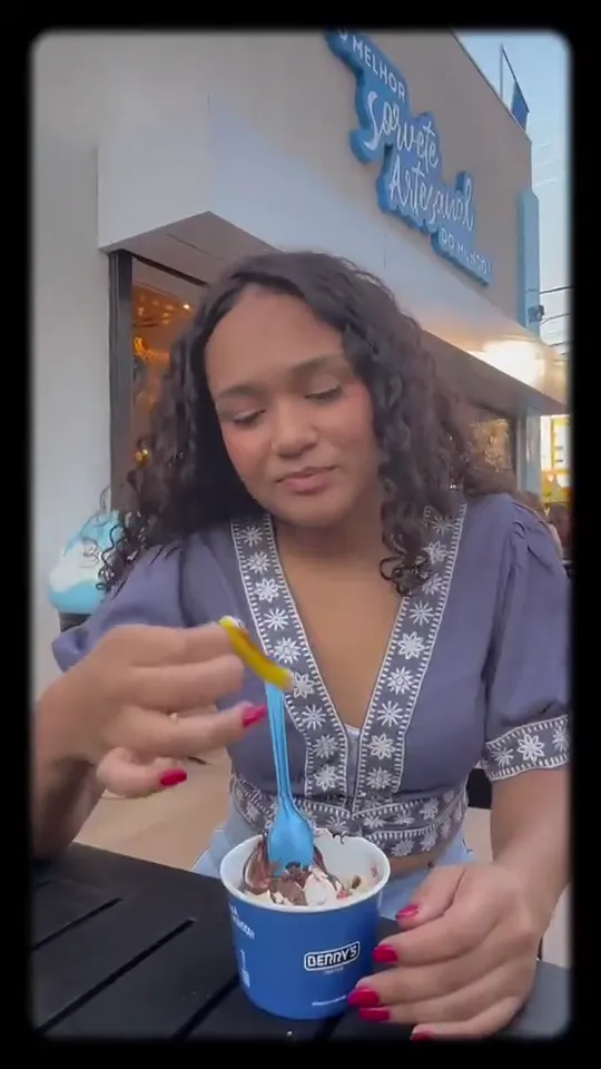 Jovem tomando sorvete na calçada de uma sorveteria antes de registrar o gasto pelo WhatsApp